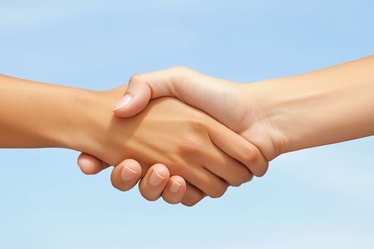Two hands clasped in a friendly handshake against a clear sky photo