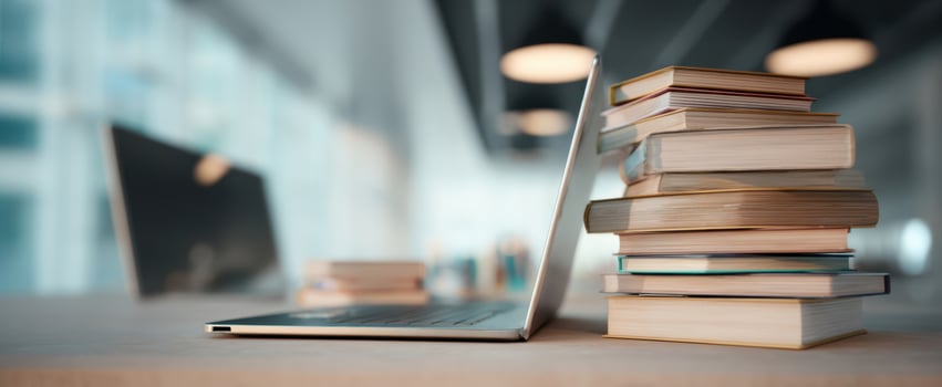 The laptop next to a neatly stacked collection of books in a modern workspace. photo