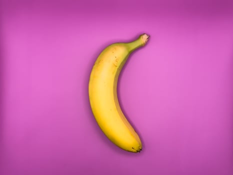 One bright yellow banana lies vertically on a purple background, top view, center of the image photo