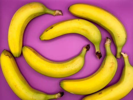 Background of bright yellow bananas lie on a purple background, top view, centered in the image photo