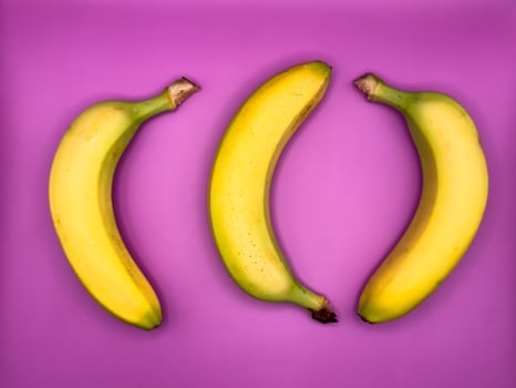 Three bright yellow bananas lie on a purple background, top view photo