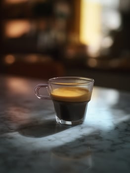 Espresso in a Glass Cup on Marble Tabletop. A close up photo of a freshly brewed espresso shot in a clear glass, ideal for coffee shop or cafe promotions.