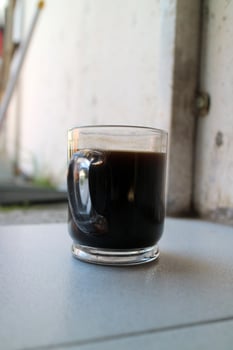 a glass of a black coffee in a glass cup photographed from the side, during the day photo
