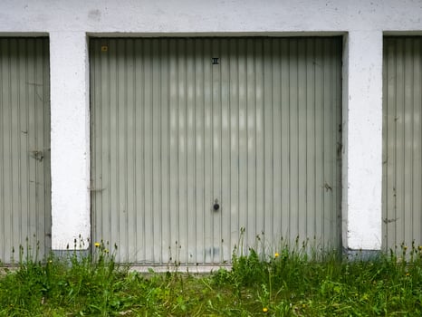 Three garage doors, with green metal panels set in concrete frames, and some greenery. photo