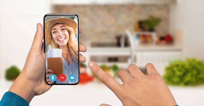 A person connects with cheerful young woman on a smartphone. The background features a cozy kitchen filled with greenery and home items. photo