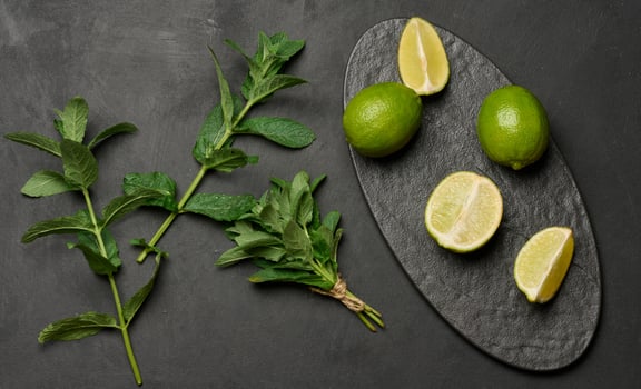 Whole and cut limes with fresh mint leaves arranged on a dark textured surface. Composition perfect for food, drink, or summer themes. photo