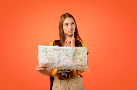 Pensive girl traveller with city map on yellow background, looking for new destination photo