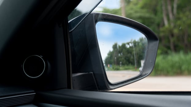 Inside view of mirrors wing. Rear view road and green trees in the daytime. Clear traffic in rural areas. photo