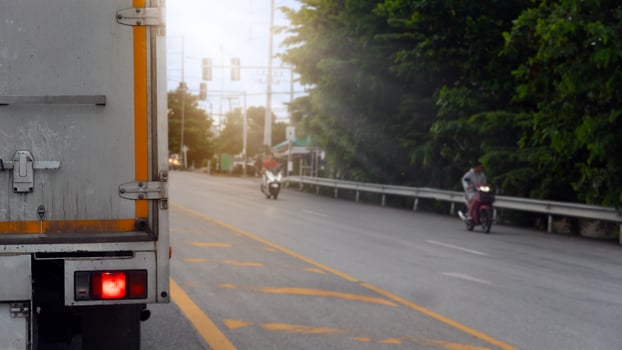 Truck car stop and turn on brake light on aspahlt road. There are yellow lines on the road. Blurred of motorcyclists on the side of the road have road barriers and trees. photo