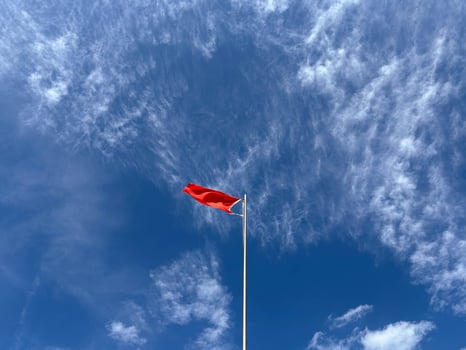 A red flag on a pole flutters in a strong wind in the blue sky. photo