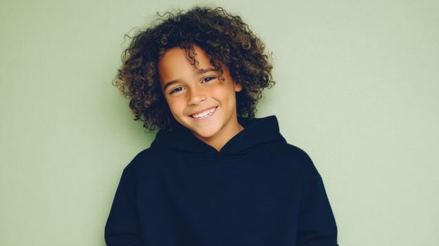 The smiling boy with curly hair wearing a hoodie against a green background. photo