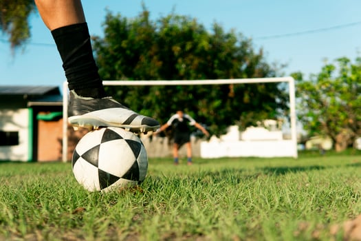 Soccer player placing their cleat on top of ball with goalkeeper in background photo