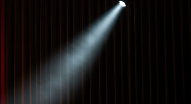 A bright spotlight illuminating a stage with dark, elegant red velvet curtains. photo