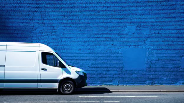 The white delivery van parked against a vibrant blue wall on a sunny day. photo