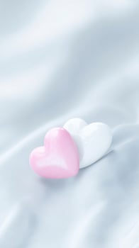 Two glossy heart-shaped objects, one pink and one white, resting on a soft, textured fabric background, symbolizing love and affection in a serene setting photo