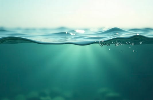 Half-underwater split view of turquoise ocean water with air bubbles and sunbeams photo