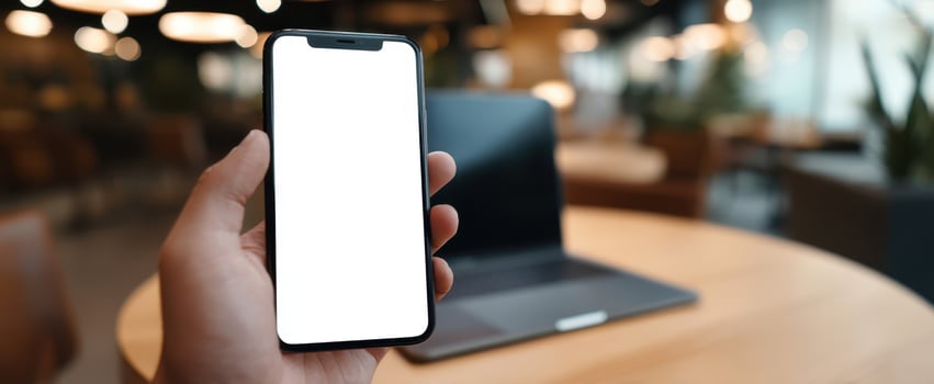 The smartphone held in hand with a blank screen in a modern workspace. photo