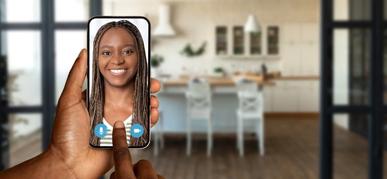A person holds a smartphone while initiating a call at home. The background features a well-furnished kitchen, showcasing the connection technology provides in everyday life. photo