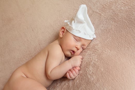 Cute little naked newborn child in a white cap lies on a soft sheet photo
