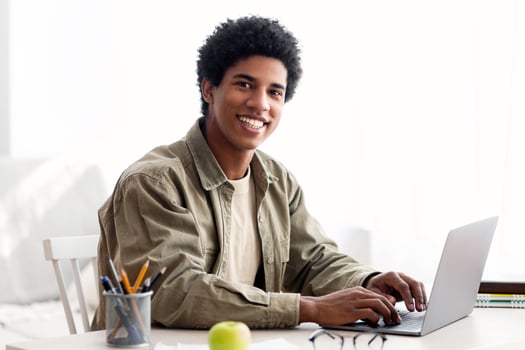 Remote schooling concept. Black teen guy typing on laptop computer during his online studies at home. Handsome African American student using PC to participate in webinar or web lecture photo
