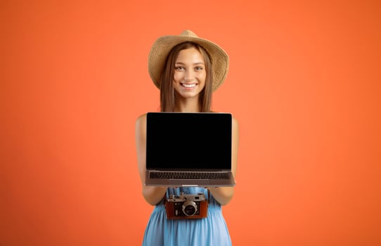 Happy young woman traveller holding laptop with blank screen over yellow studio background, website for travellers and tourists concept. Smiling lady tourist showing empty screen on her notebook photo