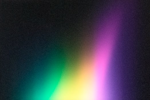 Colorful gradient background blending green, yellow and purple on grainy black surface photo