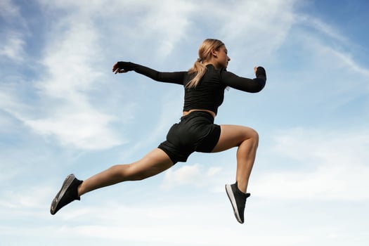 Jumping, against the sky. Beautiful fitness woman in sport clothes is outdoors photo