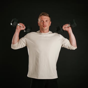 Powerful sportsman, is holding dumbbells. Against background in the studio photo