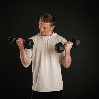 Powerful sportsman, is ,,holding dumbbells. Against background in the studio photo