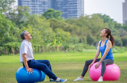 senior father with young adult daughter in sportswear resting and sitting on yoga ball,having fun after exercise in the city park photo