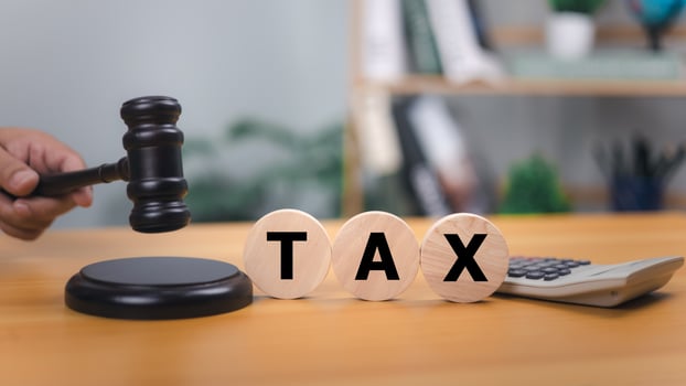 Wooden gavel and the word TAX on round blocks on a wooden desk, symbolizing tax law, legal judgment, financial decisions, with a calculator in the background and office supplies in a blurred setting. photo