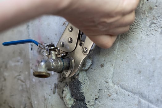 A man uses an adjustable wrench to tighten a metal faucet on a concrete wall photo
