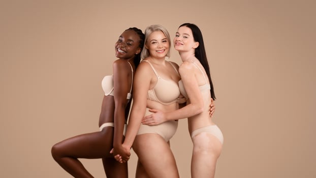 In love with myself. Three different body positive ladies posing in underwear over brown background in studio, portrait of happy females with various size and appearances smiling at camera, free space photo
