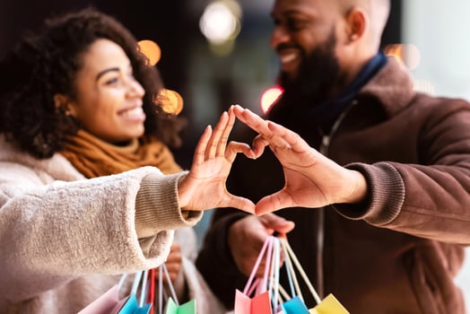Romance And Bonding Concept. Portrait of happy smiling black african american man and woman lovers making heart shape with hands walking together in the evening after shopping, holding bags photo