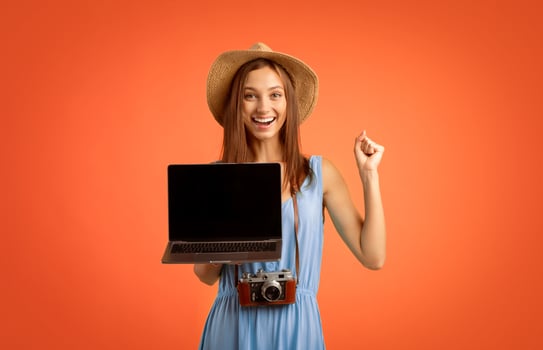 Cheerful girl traveller holding laptop with empty screen over yellow background, website for travellers and tourists photo