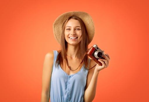Smiling female photographer posing with camera over yellow studio background photo