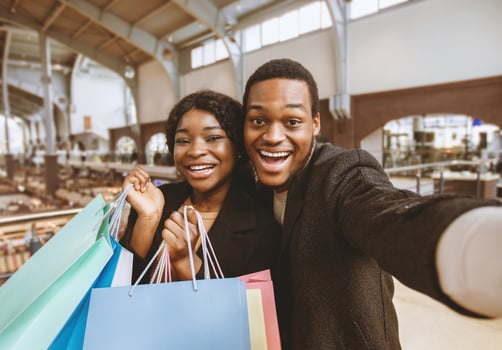 Amorous dates with shopping bags in modern city mall. Portrait of young smiling african american male and female talking during sale on weekend and make selfie at Black Friday and have fun, copy space photo