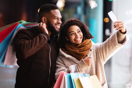 Couple Selfie. Portrait of happy casual african american woman and man taking picture on the street near mall, smiling at camera, holding colorful shopping bags with purchases. Family Photo