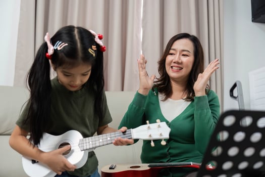 Joyful Music Lesson. Young girl learning ukulele with supportive mother at home. photo
