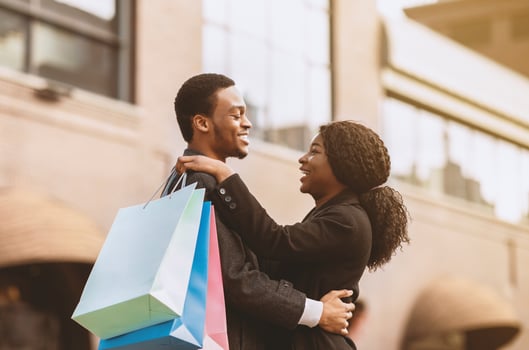 Portrait of lovely happy couple in autumn. Young attractive african american man and woman hugs, holds colorful paper shopping bags during big season sale and Black Friday, side view, copy space photo