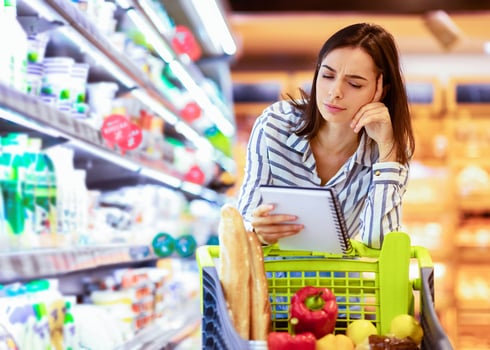 Pensive Woman Holding Grocery Shopping Checklist, Looking In Notebook, Reading Notes, Buying Products, Standing With Trolley Cart In Supermarket. Young Millennial Lady Thinking About Purchase photo