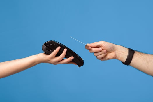Unrecognizable male and female hands with credit card and money terminal over blue studio background. Young guy making contactless payment during coronavirus pandemic, closeup photo