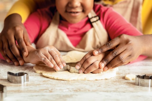 Closeup Shot Of Little Black Girl Cutting Out Heart Shape Of Dough While Baking With Mom In Kitchen, African American Family Mother And Daughter Enjoying Cooking At Home Together, Cropped Image photo