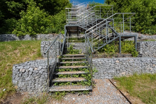 There is a beautifully designed set of stairs that gracefully leads up to a solid stone wall situated within a picturesque park, making it an inviting place to stroll and enjoy nature photo