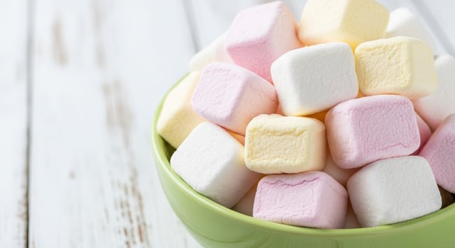 Close up of soft pastel cube marshmallows in a green bowl on a white wooden surface photo