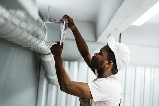 Worker performs maintenance on ventilation system in commercial building during daylight hours photo