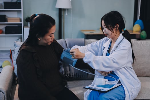 A woman is sitting on a couch with a doctor checking her blood pressure photo