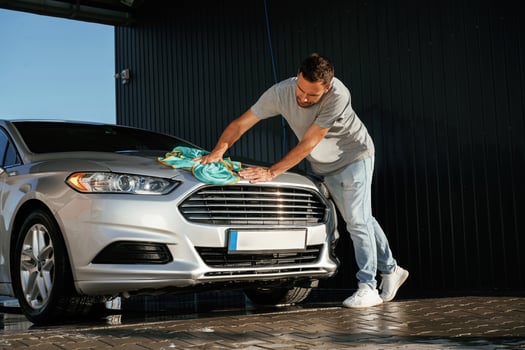 With cloth in hands.. Car wash. Man is with automobile outdoors photo