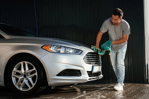 Guy, is ,polishing the surface of automobile by using cloth. Man is with his car outdoors photo