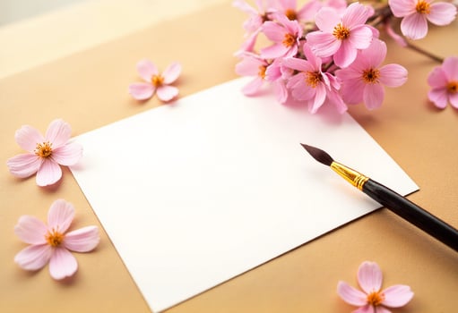 A blank paper with a brush and pink flowers on a brown background photo